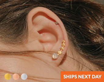 May include: Gold crescent moon earrings with a small round gemstone earring. The earrings are shown in a person's ear.