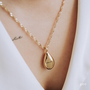 May include: A gold chain necklace with a teardrop-shaped pendant. The pendant has the inscription "1944-2020" engraved on it.