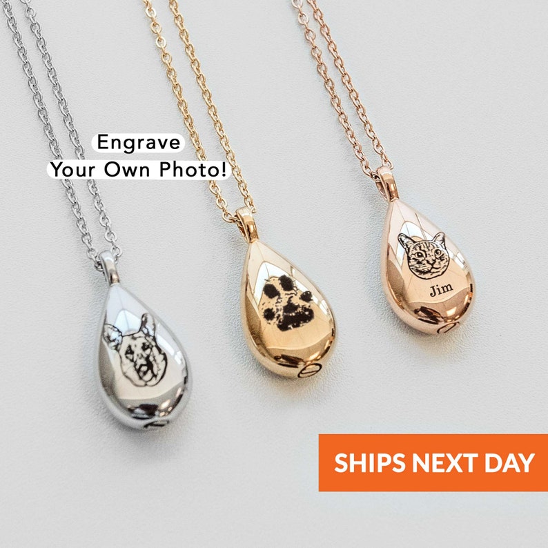 May include: Three teardrop-shaped pendant necklaces in silver, gold, and rose gold. Each pendant features an engraved design: a dog, a paw print, and a cat with the name "Jim." The text "Engrave Your Own Photo!" is visible.