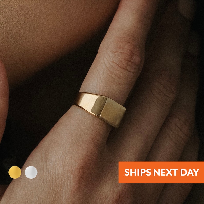 Puede incluir: Un anillo de sello de oro con una parte superior plana y rectangular.