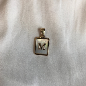 May include: Gold pendant with a white mother of pearl square charm featuring the letter M.