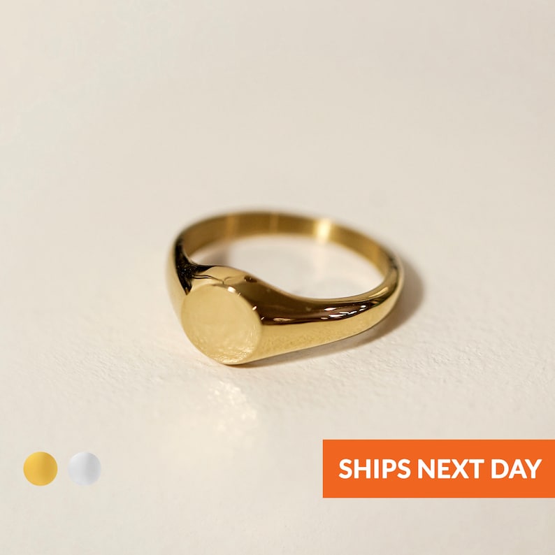 Op de afbeelding: Een gouden zegelring met een gladde, ronde bovenkant. De ring is gemaakt van metaal en heeft een gepolijste afwerking.