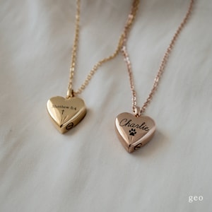 May include: Two gold heart-shaped necklaces with engraved inscriptions. One necklace has a cross and the inscription "Matthew 6:4". The other necklace has a paw print and the inscription "Charlie".