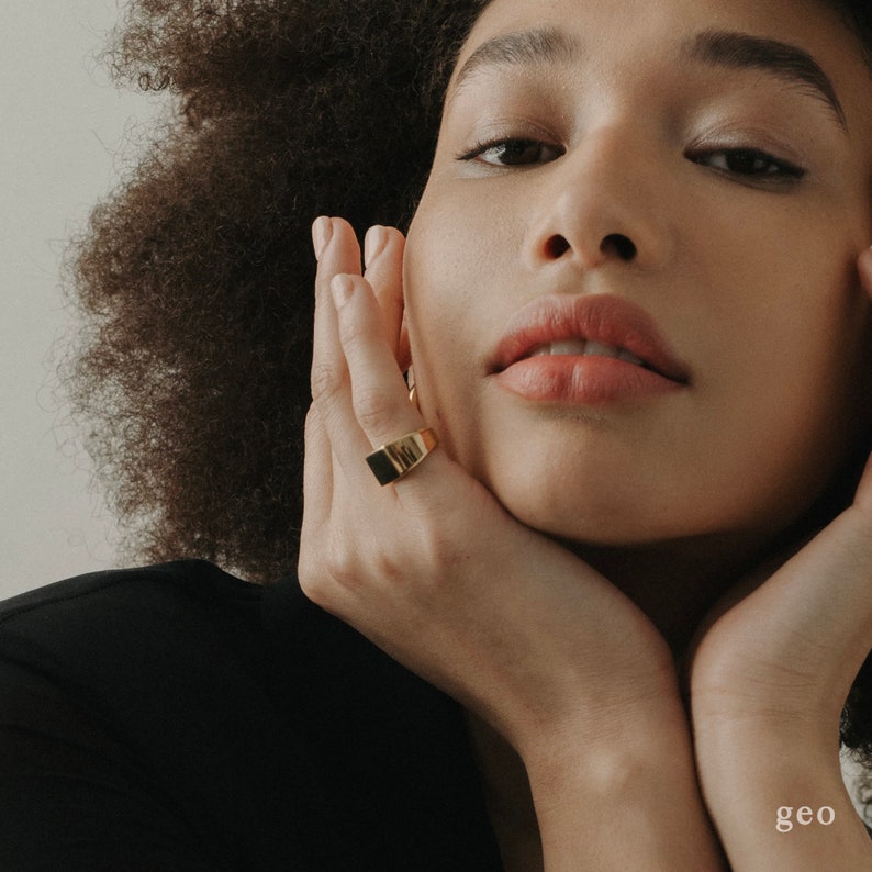 Puede incluir: Primer plano de la cara de una persona con un anillo de sello de oro en el dedo. El anillo es de dise&ntilde;o simple y rectangular.