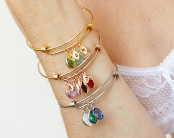 May include: A stack of five gold, rose gold, and silver charm bracelets with dangling charms featuring different colored gemstones and initial letters.