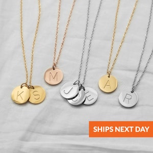 May include: Four gold necklaces with initial pendants. The necklaces are on a white surface. The pendants are round and have the letters K, S, J, C, E, A, and R engraved on them.  SHIPS NEXT DAY.
