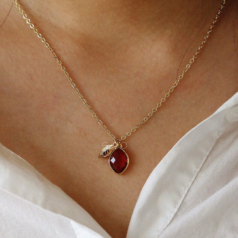 May include: A gold chain necklace with a red gemstone pendant and a small gold leaf charm.
