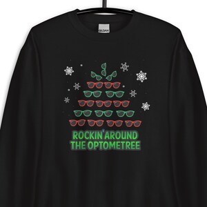May include: Black sweatshirt with a Christmas tree design made of sunglasses. The text "Rockin' Around The Optometree" is printed below the tree.