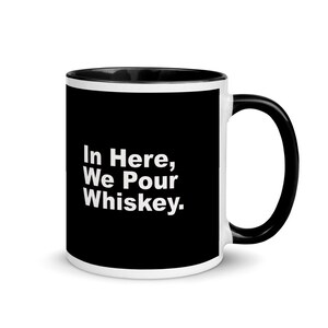 Puede incluir: Taza de cerámica blanca con borde y asa negros. La taza tiene un fondo negro con el texto "In Here, We Pour Whiskey." impreso en blanco.