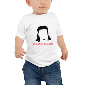 May include: White baby onesie with a black silhouette of a person with long hair and a mustache. The text "GANG GANG" is printed in pink below the silhouette.