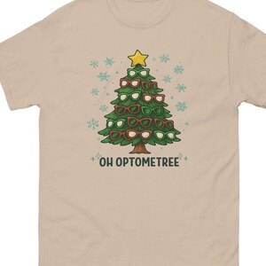 May include: Beige t-shirt featuring a Christmas tree made of eyeglasses in green and red frames, topped with a yellow star. The text "OH OPTOMETREE" is below the tree, with snowflake accents.