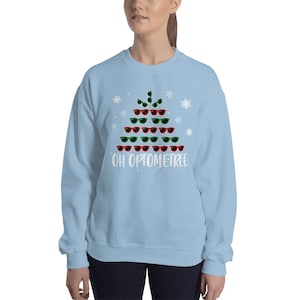 May include: Light blue sweatshirt with a white Christmas tree design made of sunglasses. The text "OH OPTOMTREE" is printed below the tree.
