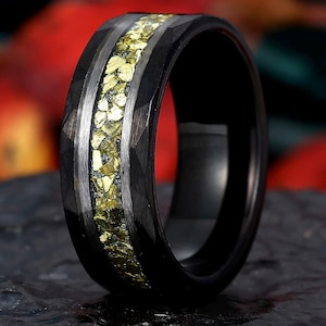 May include: A black tungsten carbide ring with a band of gold and green pyrite inlay. The ring has a brushed finish and a beveled edge.