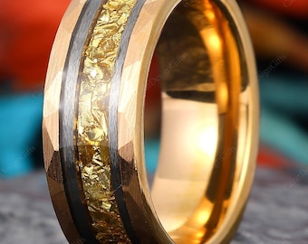 Op de afbeelding: Een goudkleurige ring met een centrale band van getextureerd goud en twee donkergrijze banden. De ring heeft een gehamerde textuur op de buitenranden. De ring wordt gepresenteerd op een donkere, getextureerde ondergrond.