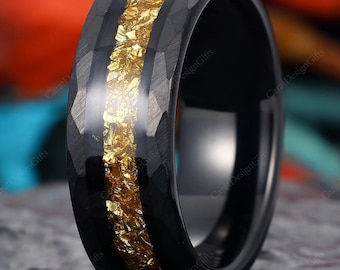 Op de afbeelding: Een zwarte ring met een gehamerde textuur en een goudkleurige inleg. De ring staat tegen een donkere achtergrond, wat het contrast tussen zwart en goud benadrukt. Het ontwerp van de ring is modern en opvallend.