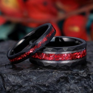 May include: Two black tungsten carbide rings with a red inlay. The rings have a beveled edge and a textured surface.