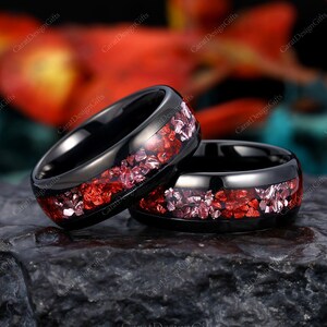 Może przedstawiać: Dwa czarne pierścionki z węglika wolframu z czerwono-różowym brokatem. Pierścionki są ułożone jeden na drugim.