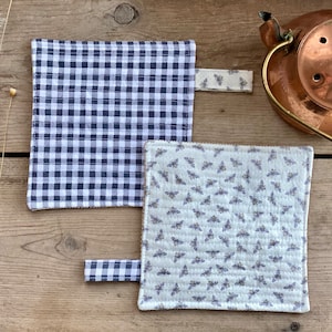 May include: Two quilted pot holders. One is white with a black bee pattern and the other is white with a black and white gingham pattern.