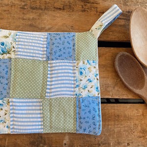 May include: A blue and green patchwork pot holder with a floral design and a hanging loop.
