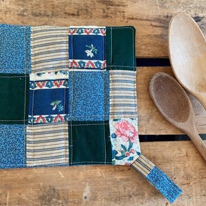 May include: A blue and green patchwork pot holder with a floral design and a hanging loop.