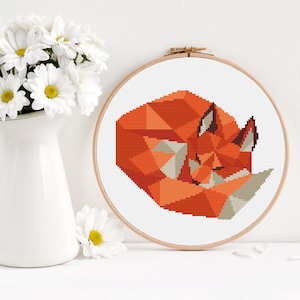 Puede incluir: Un patrón de punto de cruz de un zorro geométrico acurrucado durmiendo. El zorro es naranja y marrón sobre un fondo blanco.