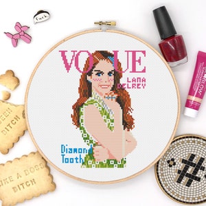 Könnte beinhalten: Ein Kreuzstich-Stickrahmen mit weißem Hintergrund und einem rosa-blauen Vogue-Magazin-Cover mit Lana Del Rey. Der Titeltext lautet "Diamond Tooth" und "Lana Del Rey".