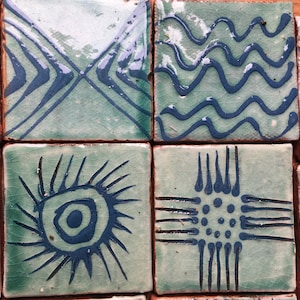 May include: Four square ceramic tiles with different blue and white geometric patterns. The patterns include a sunburst, a cross with dots, wavy lines, and intersecting lines.