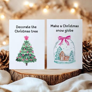 May include: Two Christmas cards with festive illustrations. One card reads "Decorate the Christmas tree" and shows a decorated tree. The other says "Make a Christmas snow globe" and depicts a snow globe with a house and trees inside.