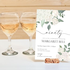 Puede incluir: Una tarjeta de invitación blanca con un diseño floral con rosas blancas y hojas verdes. El texto de la tarjeta dice "ninety" y "Join us for a celebration honouring MARGARET BELL". La fecha y hora del evento se enumeran como "Sunday, August 20th | 3:00pm". La ubicación se enumera como "Any Banquet Hall, 123 Event Rd, Anytown". La información de RSVP es "Emilis Bell (555) 873-1936".