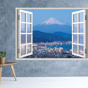 Puede incluir: Un marco de ventana blanco con vista al monte Fuji y el horizonte de una ciudad. La ventana está abierta y la vista está enmarcada por los cristales.