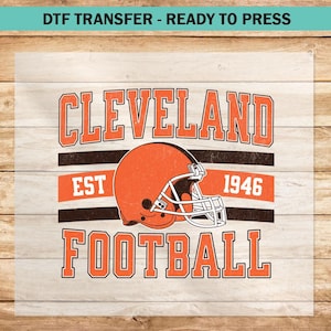 May include: An iron-on transfer design in brown and white featuring the text "Cleveland Football" with a brown football helmet graphic and the text "Est 1946".