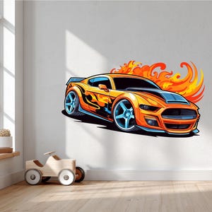 Puede incluir: Un coche naranja de dibujos animados con ruedas azules y llamas, sobre una pared blanca. El coche tiene un capó negro y es una ilustración vibrante. Ideal para la habitación de un niño o un entusiasta de los coches.