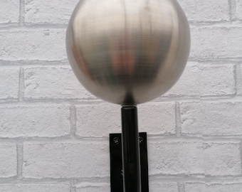 May include: A silver metal sphere mounted on a black metal bracket. The sphere is attached to the bracket with a black metal rod.
