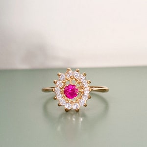 Puede incluir: Un anillo de oro con una piedra preciosa rosa rodeada de piedras transparentes.