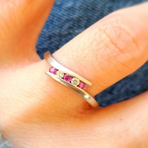 May include: A silver ring with a curved design featuring pink and clear gemstones.