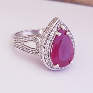 May include: A silver ring with a pear-shaped ruby gemstone surrounded by smaller white gemstones.