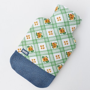 Può includere: Una fodera per borsa dell'acqua calda con un motivo a quadri verdi e bianchi e accenti floreali arancioni. La parte inferiore è in denim blu. Una piccola etichetta rettangolare con la scritta "keep LEFT" è cucita.