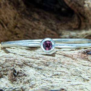Könnte beinhalten: Ein schlichter Silberring mit einem kleinen, runden, dunkelrosa Edelstein.