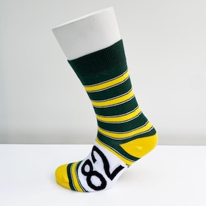 May include: A green and yellow striped sock with the number 82 in black on the white toe area. The sock is displayed on a white mannequin leg. The sock has a green cuff and yellow and green stripes.