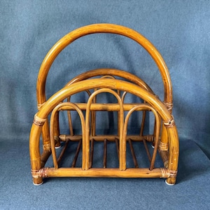 May include: A vintage bamboo magazine rack with a curved handle. The rack features a series of arched supports and a rectangular base. The natural bamboo color and design give it a retro aesthetic.