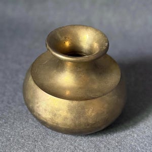 May include: A small, antique brass vase with a rounded body and a flared rim. The vase has a smooth, polished surface and a warm, golden color. The vase is likely used for decorative purposes.