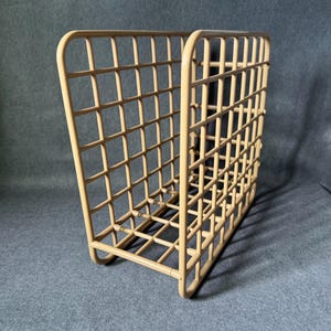 May include: A tan metal magazine rack with a grid design. The rack has a rectangular shape with rounded corners and a sturdy base. The grid pattern is made of evenly spaced vertical and horizontal bars, creating a series of small squares.