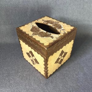 Può includere: Scatola per fazzoletti quadrata e decorativa. Dipinta in beige chiaro con dettagli marroni. La parte superiore presenta un'apertura ovale per l'erogazione dei fazzoletti. I lati sono decorati con un motivo a forma di croce. Altezza circa 12 cm.