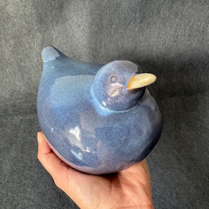Op de afbeelding: Een blauw keramiek vogeltje met een witte snavel. Het vogeltje zit op een hand.