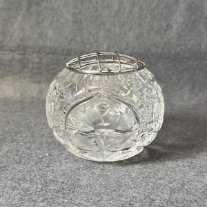 Pode incluir: Uma caneca de cerâmica branca com uma alça preta e o texto "But First, Coffee" em negrito preto. A caneca está sobre um fundo desfocado, destacando seu design limpo.