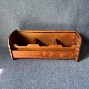 May include: A wooden desk organizer with a warm brown finish. The organizer has a rectangular shape with curved sides and multiple compartments for storing items. The design is simple and functional.