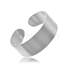 以下が含まれることがあります： ミニマリストデザインのシルバーカラーのトーリング。 幅広のオープンバンドとブラッシュ仕上げが特徴です。 調節可能なデザインで快適なフィット感を実現。 白い背景に表示されています。