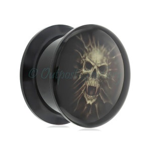 May include: Black ear plug with a skull design. The plug has a rounded face with a detailed illustration of a screaming skull against a dark background. The plug is made of a shiny black material.