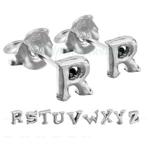 Pode incluir: Brincos de botão de prata com a letra "R". Os brincos têm a forma da letra "R" e têm um acabamento polido. Outras letras do alfabeto são exibidas abaixo. Os brincos são pequenos e delicados.