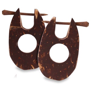 May include: A pair of dark brown, coconut shell earrings. Each earring has a unique shape with a large, central hole and a wooden stick for insertion. The earrings are displayed against a white background.
